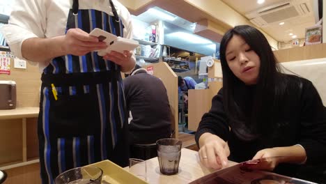 Young-Japanese-woman-ordering-food-from-waiter-inside-typical-Japanese-fast-food-restaurant