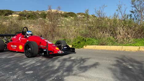 Roter-Rennwagen,-Der-Langsam-Auf-Einer-Testfahrt-Am-Hügel-In-Imtahleb-Malta-Vorbeifährt-–-Mittlere-Aufnahme