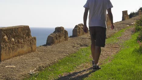 Man-walking-on-cliff-path-with-view-of-ocean