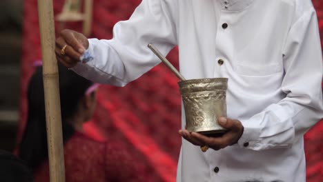 Hindu-priest-dressed-in-white-uses-a-small-flower-to-gather-water-from-cup-and-sprinkle-over-believers-at-an-outdoor-ceremony