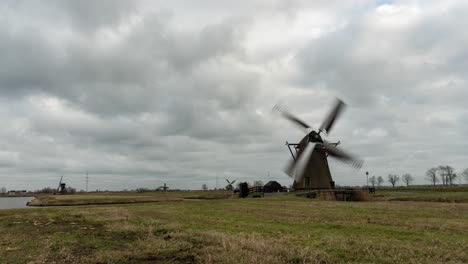Dutch-windmills-turning-in-wind-on-overcast-day,-landscape-time-lapse