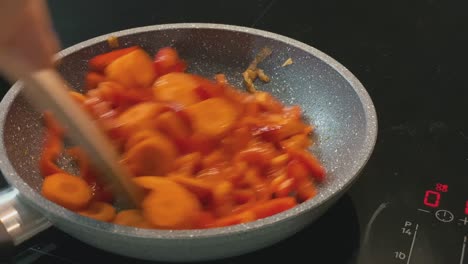Quickly-stirring-and-mixing-cooked-carrots-and-peppers-with-a-wooden-spatula