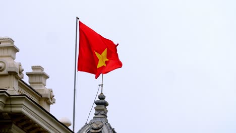 Hanoi-Opera-House-rooftop-with-the-Vietnamese-Flag-waving-in-slow-motion,-Square-of-August-Revolution,-Zoomed-in-shot