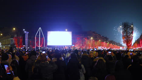 Fireworks-during-the-arrival-of-on-Paris'-main-Champs-Ã‰lysÃ©es,-surrounded-by-a-crowd-of-people-on-the-main-street-with-a-view-of-the-Triumphal-Arch-and-a-red-covered-street