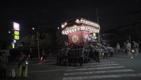 People-pushing-traditional-japanese-festival-car-through-street-at-night