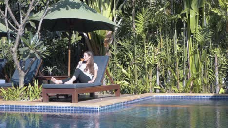 Long-Shot-of-a-Young-Lady-Relaxing-on-a-Sun-Lounger-by-the-Pool-Drinking-a-Cocktail-at-a-Tropical-Hotel