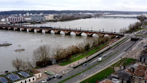 Panning-shot-of-the-city-showing-Pont-de-Pierre,-Garonne-river,-Basilica-of-Saint-Michael-and-City-gate-while-snowing-slightly,-Aerial-pan-right-reveal-hovering-shot
