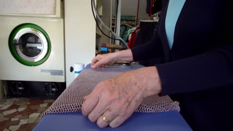 Older-woman-ironing-a-folded-garment-at-a-laundromat-store,-locked-tripod-shot