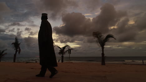 An-African-man-wearing-dashiki-walks-past-on-Senegambia-Beach-Serrekunda-The-Gambia-at-sunset-right-to-left