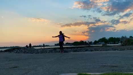 Asian-lay-showing-her-joy-of-happiness-by-jumping-and-dancing-on-a-platform-with-sunset-at-the-background