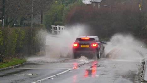 SUV-driving-and-splashing-through-stormy-flash-flooded-road-corner-bend-UK