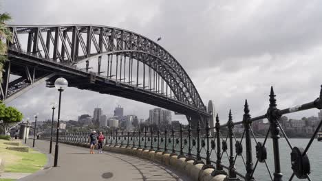 Sydney,-New-South-Wales,-Australia---People-Walking-Under-The-Sydney-Harbour-Bridge-On-A-Sunny-Day---Wide-Shot