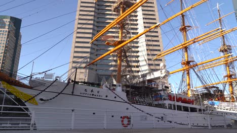 Person-With-Backpack-Walking-In-Front-Of-Nippon-Maru-Ship-In-Yokohama-Harbor-In-Japan---High-Rising-Building---Low-Angle-Shot