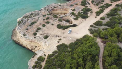 Fontainhas-Beach-in-the-south-of-Portugal-with-camping-van-parked-on-top-of-sea-carved-caves,-Aerial-approach-tilt-down