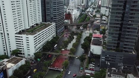 Bangkok,-Tailandia,-Metrópolis-Moderna-Midtown-Antena,-Tráfico-De-Bulevar-Entre-Rascacielos-Y-Tren-Bts-Skytrain-En-Tren-Con-Curvas