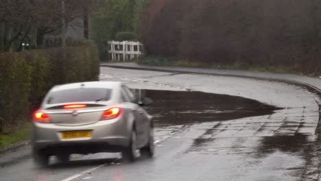Silbernes-Auto,-Das-Durch-Eine-Stürmische,-Von-Sturzfluten-überschwemmte-Straßenecke-In-Großbritannien-Planscht