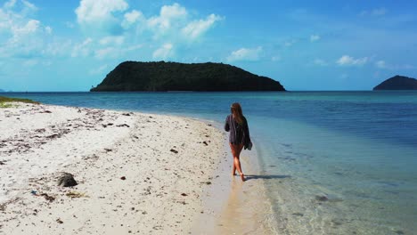 Lonely-unrecognizable-woman-walking-on-white-sandy-beach-alongside-calm-clear-water-of-shallow-lagoon,-tropical-islands-in-thailand