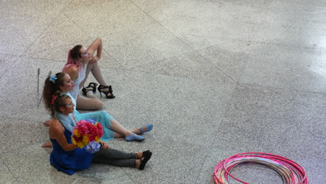 Three-girls-sitting-on-floor,-watching,-applauding-and-having-fun,-hoops-on-floor,-street-circus-show