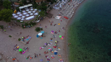Drone-flies-over-the-corner-of-a-crowded-beach-and-slowly-tilts-up-to-reveal-beautiful-mountains