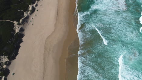 Aerial---Gentle-waves-running-onto-pristine-beach,-ascending-top-down-shot