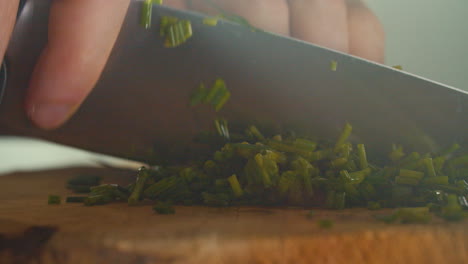 Close-shot-of-a-male-hand-cutting-chives-on-a-wooden-cutting-board-in-a-smoky-kitchen-atmosphere,-nice-sun-streaks