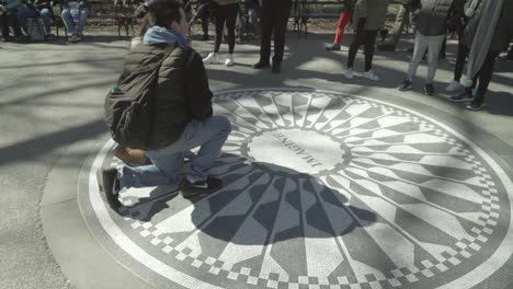 Two-people-kneeling-down-at-the-John-Lennon-Memorial-in-Central-Park,-Manhattan,-so-they-can-have-a-photo-taken