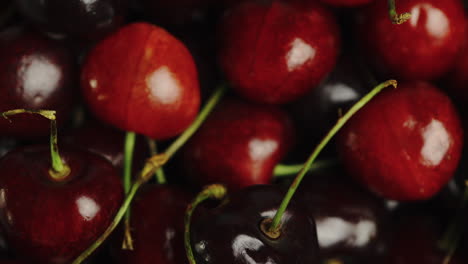 Close-Up-of-bright-red-cherries-in-a-bowl,-firstly-being-picked-up-and-then-being-dropped-back-in