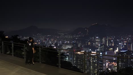 Pareja-Coreana-Teniendo-Una-Cita-En-La-Torre-Namsan-Viendo-La-Noche-En-Seúl-Y-Tomando-Fotografías-En-El-Fondo-De-La-Ciudad