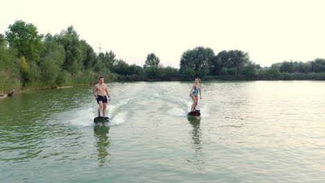 A-young-couple-having-some-extreme-fun-riding-jetsurf-boards-together,-aerial-dolly,-slow-motion