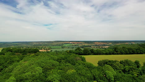 Aerial-shot-over-a-forest-and-English-agricultural-land,-on-a-bright-sunny-day
