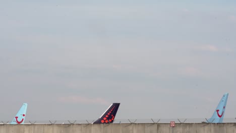 Aircrafts-of-TUI-Airways-and-Brussels-Airlines-rising-above-a-barbed-wire-wall-with-their-fins