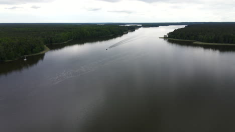 Drone-shot-of-fast-moving-motorboat-in-the-distance-on-lake-with-white-trail-leaving-behind