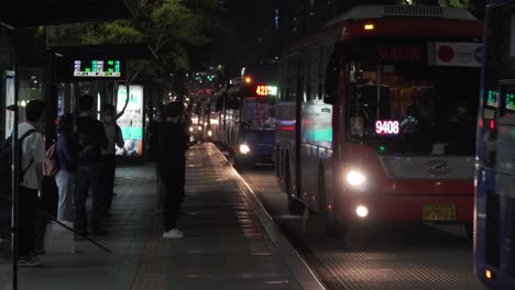 Gente-Coreana-Esperando-Autobuses-En-La-Estación-De-Autobuses-En-El-Distrito-De-Gangnam,-Seúl-Por-La-Noche---Plano-Medio