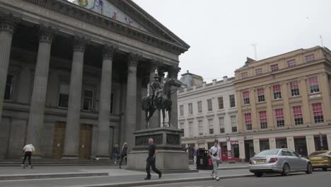 A-slow-motion,-wide-shot-of-people-walking-and-practising-their-skateboarding-skills,-next-to-the-Duke-of-Wellington-statue