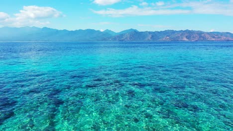 Agua-Cristalina-Esmeralda-De-Una-Laguna-Azul-Poco-Profunda-Con-Arrecifes-De-Coral-Y-Guijarros-Bajo-El-Agua,-Cielo-Brillante-Con-Nubes,-Bali