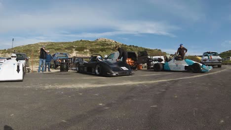 A-Woman-Checking-On-The-Black-Racing-Car-Parked-At-The-Roadside-Of-The-Hill-In-Imtahleb-Malta-Under-The-Blue-Sky---GoPro-Pan-Shot