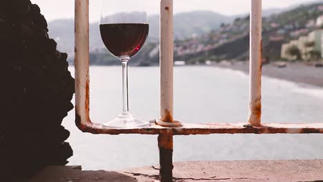 Glass-of-red-wine-on-terrace-railing-overlooking-Madeiran-coastline-and-mountains