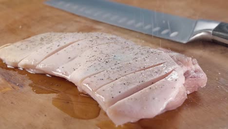 Close-Slider-Shot-in-Slow-Motion-of-Grinding-Salt-on-a-Oiled-and-Scored-Raw-Belly-Pork-On-a-Wooden-Chopping-Board