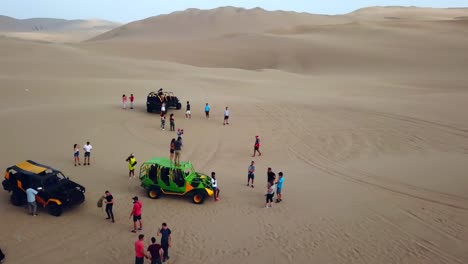 Aerial,-reverse,-drone-shot,-away-from-a-group-of-people-and-4x4-buggies,-on-a-sand-dunes,-at-the-Atacama-desert,-on-a-sunny-day,-in-south-Peru