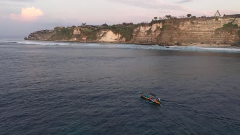 Tourists-in-the-traditional-Balinese-boat-cadik-approaching-the-fortified-cliffs-with-hidden-temple,-Pura-Luhur,-Uluwatu,-Bali,-Indonesia