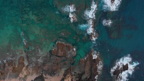 Aerial-shot-view-of-shallow-rocks-sea-shoreline-in-slow-motion