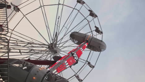Satellite-ride-at-carnival-in-Pennsylvania-with-ferris-wheel-in-background,-Vertical,-Slow-Motion