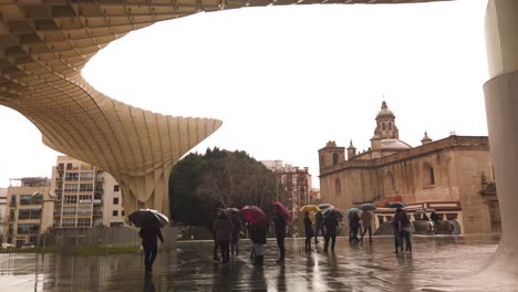 People-with-umbrellas-under-Las-Setas-in-Seville,-Spain-on-rainy-day