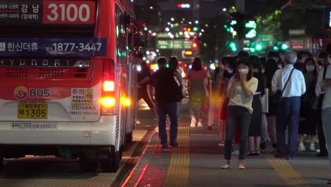 Korean-woman-wearing-face-mask-stands-by-the-bus-stop-in-Gangnam-station,-the-downtown-city-at-night,-COVID-19,-people-get-on-bus-and-get-out-of-bus,-Seoul,-South-Korea