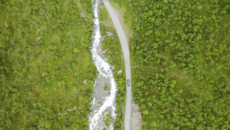 Top-down-Shot-Of-A-Car-Travelling-On-The-Road-Along-The-Narrow-River-And-Green-Landscape-In-Hemsedal,-Norway---aerial-drone