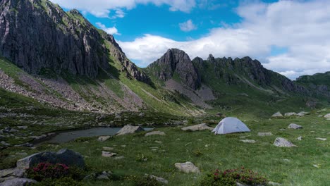 single-person-tent-in-mountain-valley-near-pond-with-passing-clouds,-timelapse