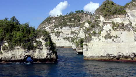 Diamond-Beach-in-Nusa-Penida-island-with-natural-rock-arch-and-tall-rock-formations,-Aerial-dolly-out-reveal-shot