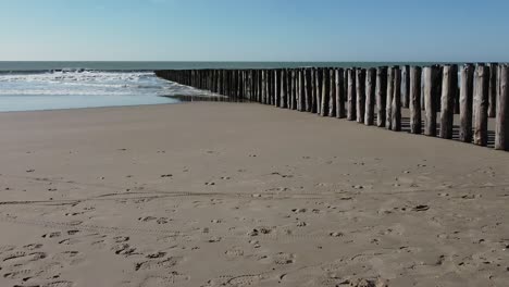 Dolly-shot-of-a-double-wooden-breakwater-on-the-beach,-blue-sky,-the-sea-and-no-people