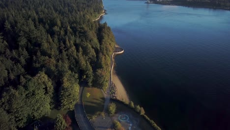 Seawall-And-Lush-Green-Coniferous-Trees-At-Stanley-Park-With-Lions-Gate-Bridge-Over-The-Burrard-Inlet-In-Vancouver,-BC,-Canada