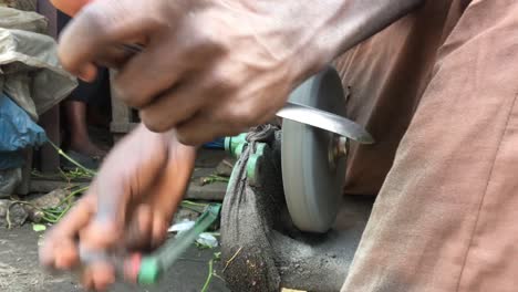Nahaufnahme-Der-Hand-Eines-Nigerianischen-Mannes,-Der-Ein-Messer-Mit-Einem-Rollenden-Schleifstein-Schärft
